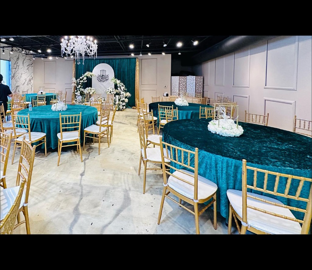 Elegant banquet hall with teal tablecloths, gold chiavari chairs, crystal chandelier, and floral stage backdrop