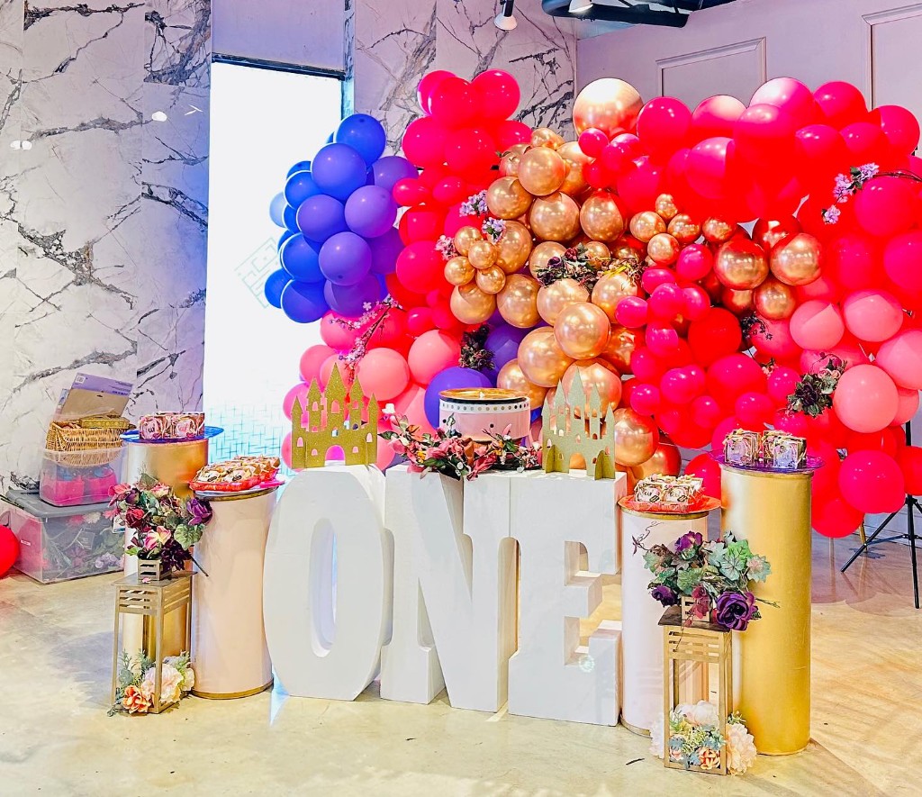 Colorful first birthday party setup with pink, purple, and gold balloon arch and castle-themed decor